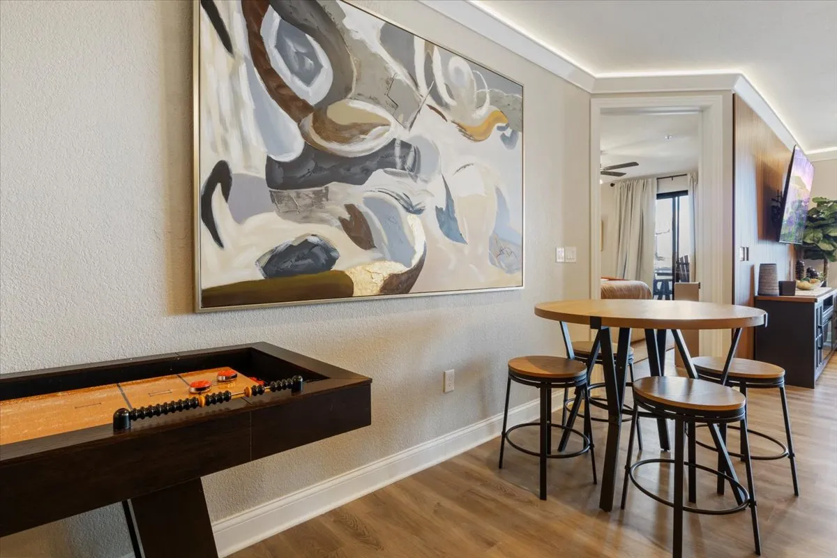 The dining area comes alive with a round dining table, abstract art, and the shuffleboard table in view. The setting is intimate and playful, ideal for memorable game nights and laughter-filled meals.