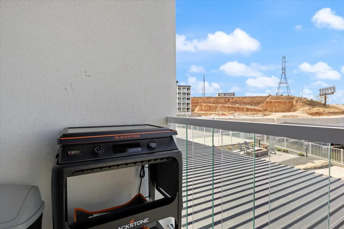 A contemporary balcony setup featuring a Blackstone grill positioned by the railing, offering sweeping views over the landscape. The space is designed for alfresco cooking and socializing, making it perfect for evening barbecues or casual weekend brunches.