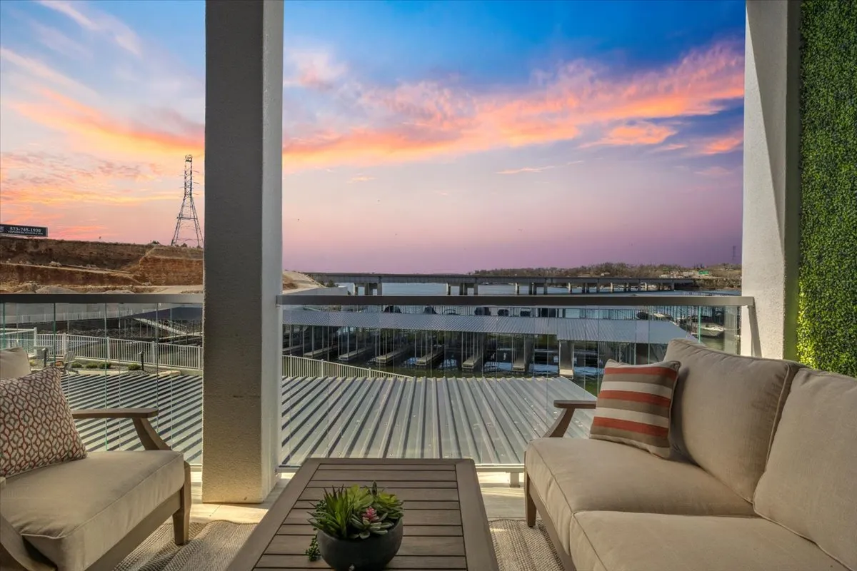The hero image showcases an inviting balcony overlooking the tranquil lake, bathed in the warm glow of a stunning sunset. Comfortable outdoor furniture is arranged for socializing or relaxing, with the serene water and expansive sky creating a dreamy lakeside backdrop. The scene evokes both the possibility of intimate dinners and quiet moments of reflection.