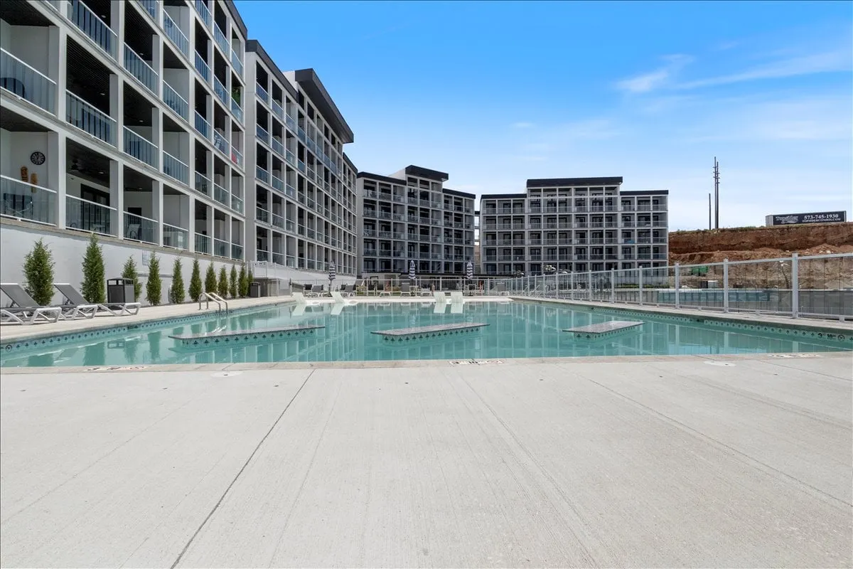 A glistening swimming pool is surrounded by modern residential buildings and comfortable lounge chairs. The area is set up for social gatherings, with the sun setting in the background, casting a warm, inviting glow over the scene. The image evokes a sense of relaxation and togetherness.