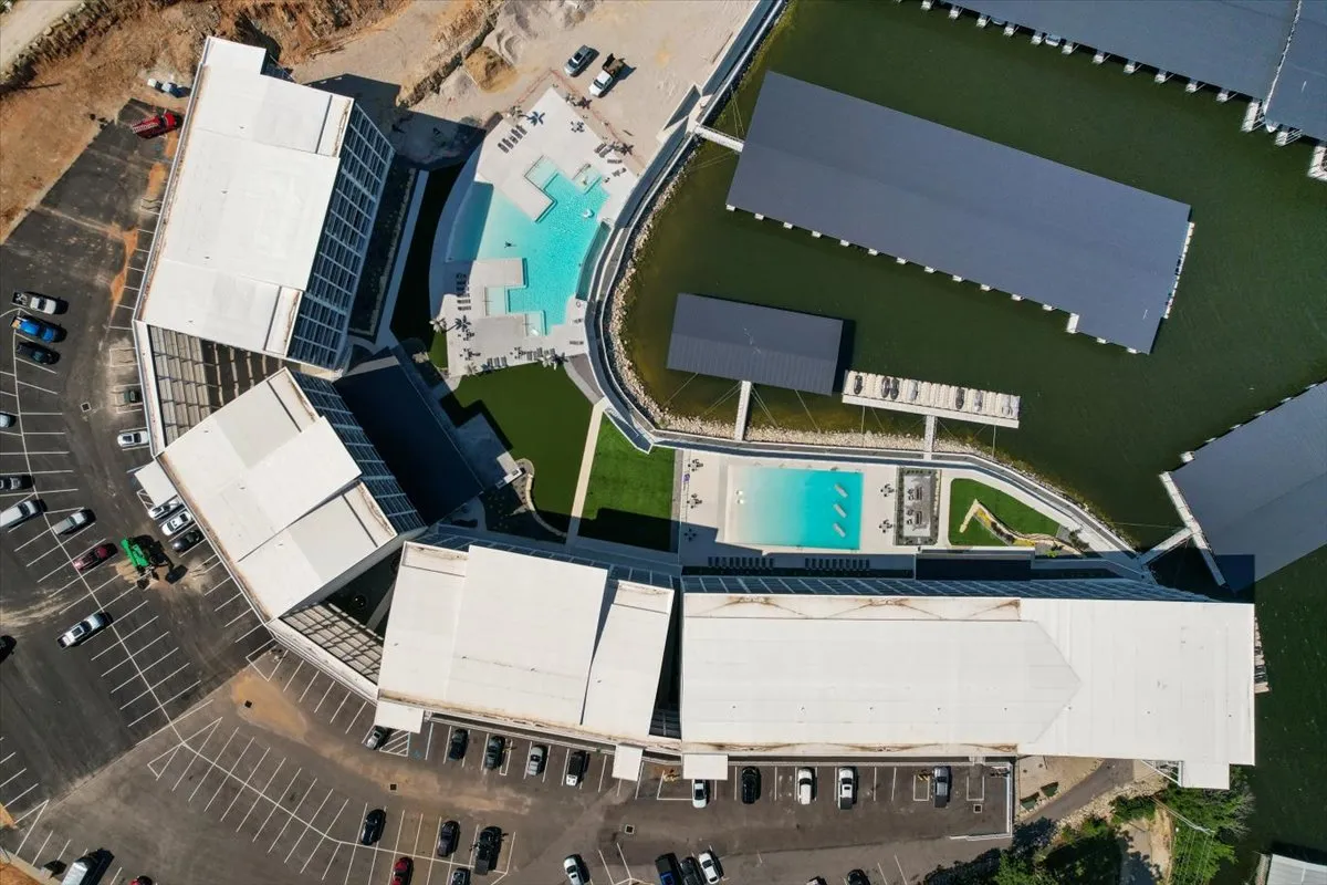 The photo features a vibrant pool area with lounge chairs, a marina with boats, and nearby buildings, all set against the backdrop of the lake. The scene exudes energy, inviting both swimming and boating, and hints at the lively social atmosphere of the resort community.